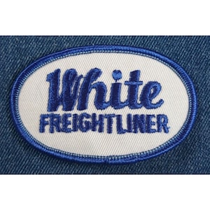 May include: White oval embroidered patch with blue stitching and the text "White Freightliner" in blue.