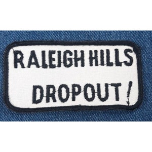 May include: White fabric patch with black embroidered text that reads "Raleigh Hills Dropout!" The patch has a black border.