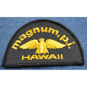 May include: A black embroidered patch with a gold eagle and the text "Magnum, p.i. HAWAII" in a curved arc.