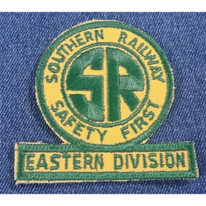 May include: A yellow and green embroidered patch with the text "Southern Railway Safety First" in a circle around the letters "SR" in a larger circle. Below the circle is a yellow and green banner with the text "Eastern Division".