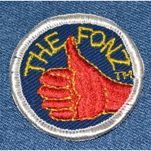 May include: A blue and white embroidered patch with a red thumbs up and the text "THE FOND TM" in yellow.