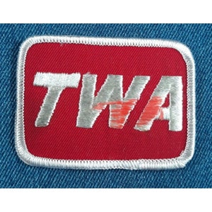 May include: A red fabric patch with a white embroidered border and the word "TWA" in white with a red "W" in the center.
