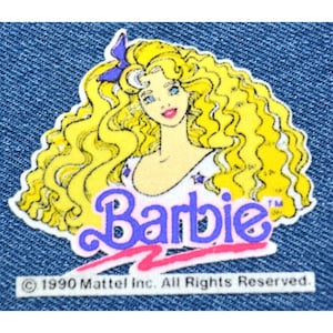 May include: A vintage Barbie patch with a yellow-blonde haired Barbie doll wearing a white shirt with stars. The Barbie logo is in purple and pink with the text "Barbie" and a trademark symbol.