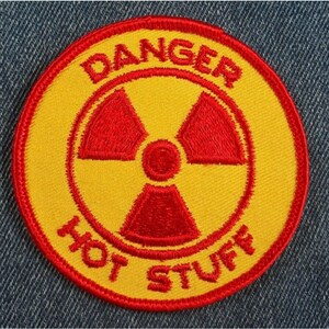 May include: A yellow and red embroidered patch with the text "DANGER HOT STUFF" and a red radiation symbol in the center.