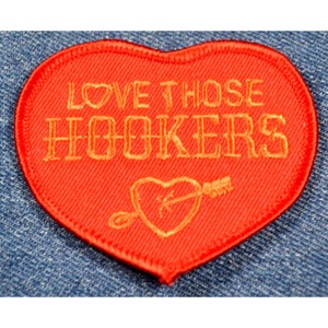 May include: Red heart-shaped patch with gold embroidered text that reads "LOVE THOSE HOOKERS" and a gold heart with an arrow through it.