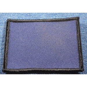 May include: A rectangular patch with a navy blue center and a black stitched border. The patch is set against a light blue denim background, showcasing its texture and design.