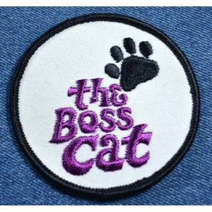 May include: White oval embroidered patch with a black paw print and the text "the boss cat" in purple.