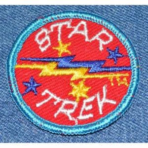May include: A red and blue embroidered patch with the words "STAR TREK" in white lettering. The patch features a yellow lightning bolt with blue accents and five stars.