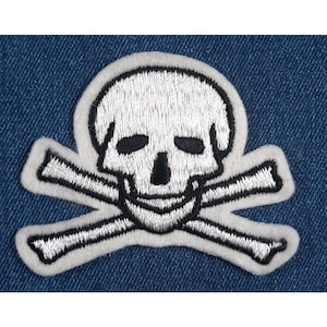 May include: White embroidered skull and crossbones patch on a blue denim background.