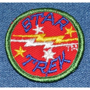May include: A red, white, and yellow embroidered patch with the words "STAR TREK" in blue lettering. The patch has a green border and features a lightning bolt design.