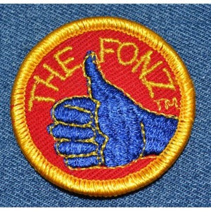 May include: A red and gold embroidered patch with a blue thumbs up hand and the text "The Fox" in yellow.