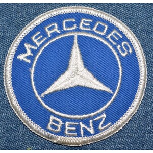 May include: A white embroidered patch with a blue background. The patch features the Mercedes-Benz logo, a three-pointed star, and the words "Mercedes-Benz" around the star.
