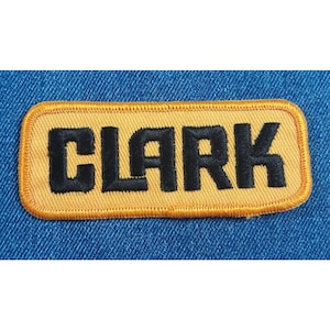 May include: A yellow rectangular patch with a black embroidered name "CLARK" on it.