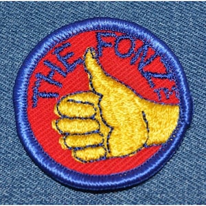 May include: A red and blue embroidered patch with a yellow thumbs up and the text "The Fonzi" in white.