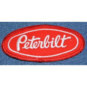 May include: Red oval embroidered patch with white stitching. The patch says "Peterbilt" in a white cursive font.