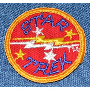 May include: A red and orange embroidered patch with the text "STAR TREK" in blue lettering. The patch features a yellow lightning bolt with white accents and five white stars.