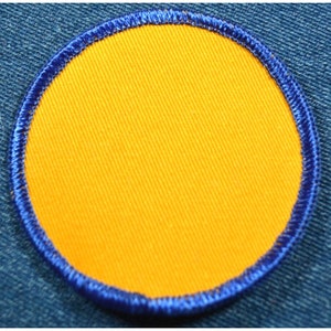 May include: A round, yellow fabric patch with a blue stitched border.
