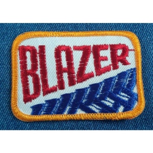 May include: A white embroidered patch with an orange border. The patch features the word "BLAZER" in red embroidery and a blue and white pattern underneath.