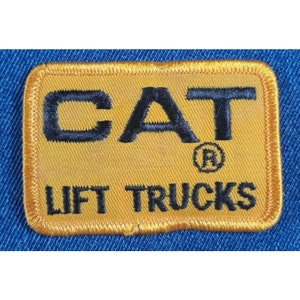 May include: A yellow embroidered patch with black stitching. The patch features the word "CAT" in large letters with a registered trademark symbol. Below the word "CAT" is the text "LIFT TRUCKS".