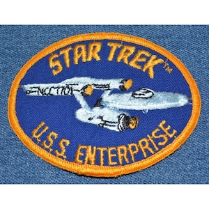 May include: A blue and orange embroidered patch with the text "STAR TREK" and "U.S.S. ENTERPRISE" and a white spaceship.