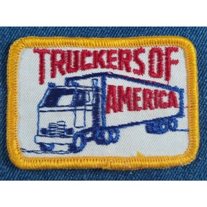 May include: Embroidered patch with the words "Truckers of America" in red thread. The patch features a blue and white truck design. The patch has a yellow border and is set against a blue denim background.