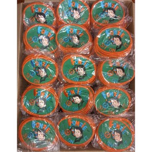Peut inclure: Une boîte remplie de patchs ovales. Chaque patch a une bordure orange et un centre vert avec les mots "FONZIE SIT ON IT" et un portrait d'homme. Les patchs sont emballés individuellement dans du plastique transparent.
