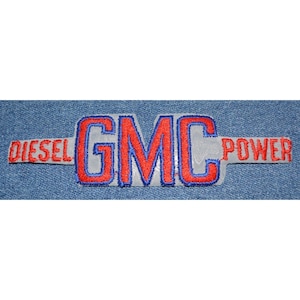 May include: Embroidered patch featuring the text "GMC" in red with a blue outline, and the words "DIESEL" and "POWER" in red. The patch has a light gray background and is set against a blue denim fabric.