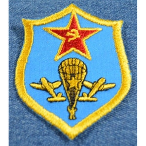 May include: A blue and gold embroidered patch with a red star and a parachute with two airplanes. The star has a red "S" in the center.
