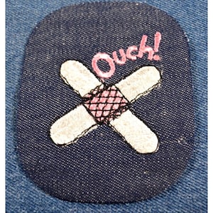 May include: A blue denim patch with a white embroidered bandage and the word "Ouch!" in pink embroidery.