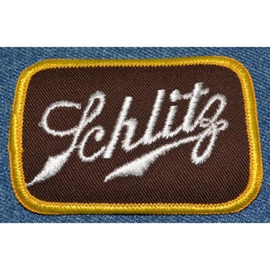 May include: A brown fabric patch with a yellow border. The word "Schlitz" is embroidered in white on the patch.