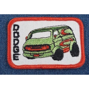 May include: A white embroidered patch with a red border featuring a green Dodge van with red and white stripes. The word "DODGE" is embroidered vertically on the left side of the patch.