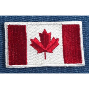 May include: A red and white embroidered Canadian flag patch. The flag features a red maple leaf on a white background with red stripes on either side.