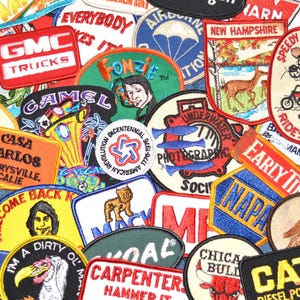 May include: A collection of embroidered patches with various designs and text. Patches include logos for GMC Trucks, Camel cigarettes, and Casa Carlos. Other patches feature cartoon characters and state emblems.