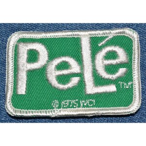 May include: White embroidered patch with the word "Pelé" in white letters on a green background. The patch has a white border and the text "TM" and "© 1975 WCI" in smaller white letters.