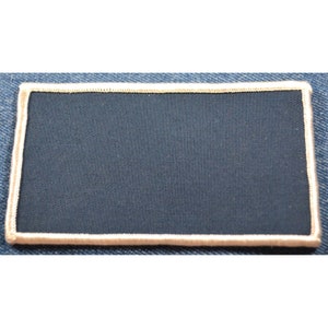 May include: A blank navy blue patch with a white border. The patch is made of fabric and has a rectangular shape.