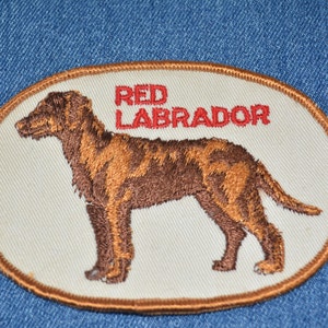 May include: An embroidered patch featuring a brown Labrador Retriever with the text "RED LABRADOR" in red lettering.