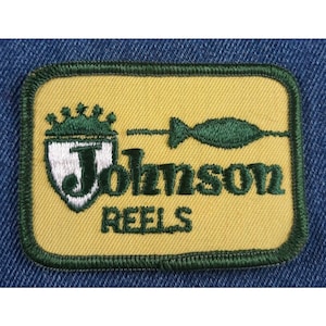 May include: A yellow and green embroidered patch with the text "Johnson Reels" and a stylized fish design.