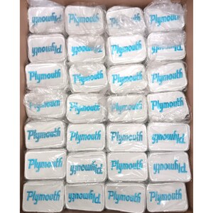 May include: A box filled with rectangular white patches. Each patch has the word "Plymouth" embroidered in a teal blue color. The patches are individually wrapped in clear plastic.
