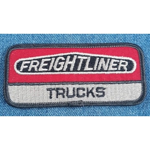 May include: A red and gray embroidered patch with the text "FREIGHTLINER TRUCKS" in black.