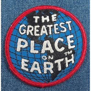 May include: Embroidered patch with a blue globe design, featuring the text "THE GREATEST PLACE ON EARTH" in white. The patch has a red border and is set against a denim background.