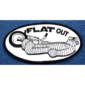 May include: White oval embroidered patch with black outline. The patch features a black and white illustration of a motorcycle with the text "FLAT OUT" above it.