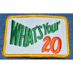 May include: A white embroidered patch with a green "What's Your" and an orange "20" surrounded by a yellow border.