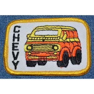 May include: An embroidered patch featuring a yellow and orange Chevy van with the word "CHEVY" in black lettering.