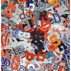 May include: A large collection of colorful felt letter patches. The patches are in various colors, including red, blue, green, orange, and white. The letters are in a variety of fonts and styles.