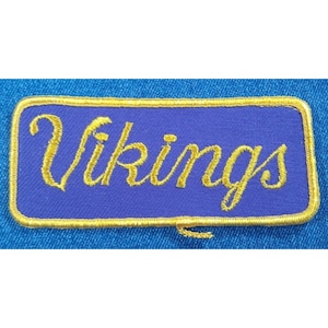 May include: A purple and gold embroidered patch with the word "Vikings" in a cursive font.