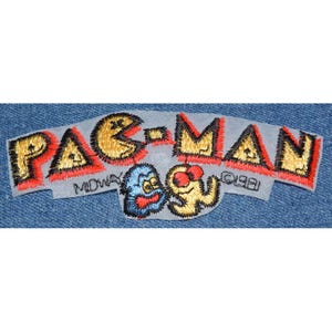 May include: A yellow and black embroidered Pac-Man patch with the text "PAC-MAN" in red and black. The patch also features the text "MIDWAY" and "©1981".