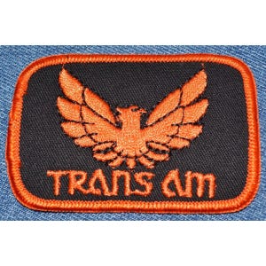 May include: Orange embroidered bird with outstretched wings on a black background with the text "TRANS AM" in orange.