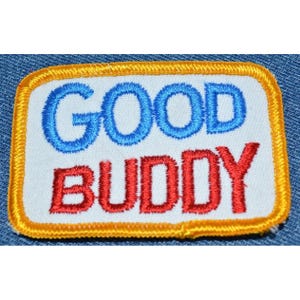 May include: A white embroidered patch with a yellow border. The patch says "GOOD BUDDY" in blue and red lettering.