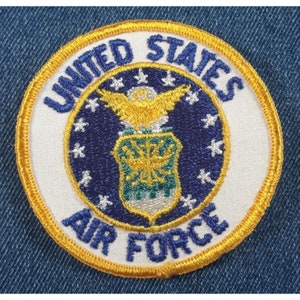 May include: A white embroidered patch with a blue and gold United States Air Force emblem. The patch has a gold border and the words "United States Air Force" are embroidered in blue.