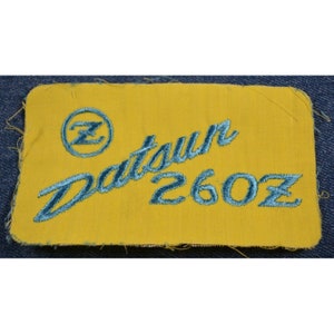May include: A yellow fabric patch with blue embroidered text that reads "Datsun 260Z" and a blue circle with a stylized "Z" inside.